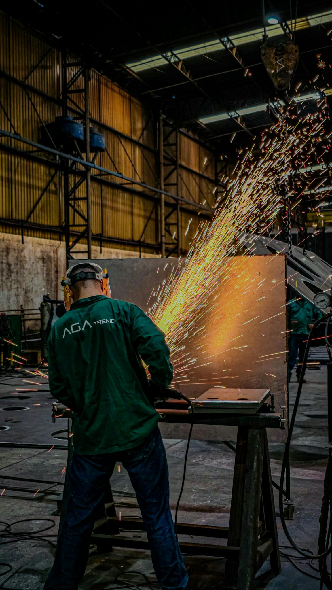 A welder in a factory uses a grinder, sending sparks flying in an industrial setting.